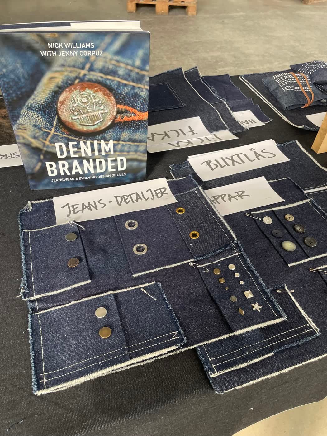Denim construction swatches with handwritten Swedish labels beside the reference book "Denim Branded".
