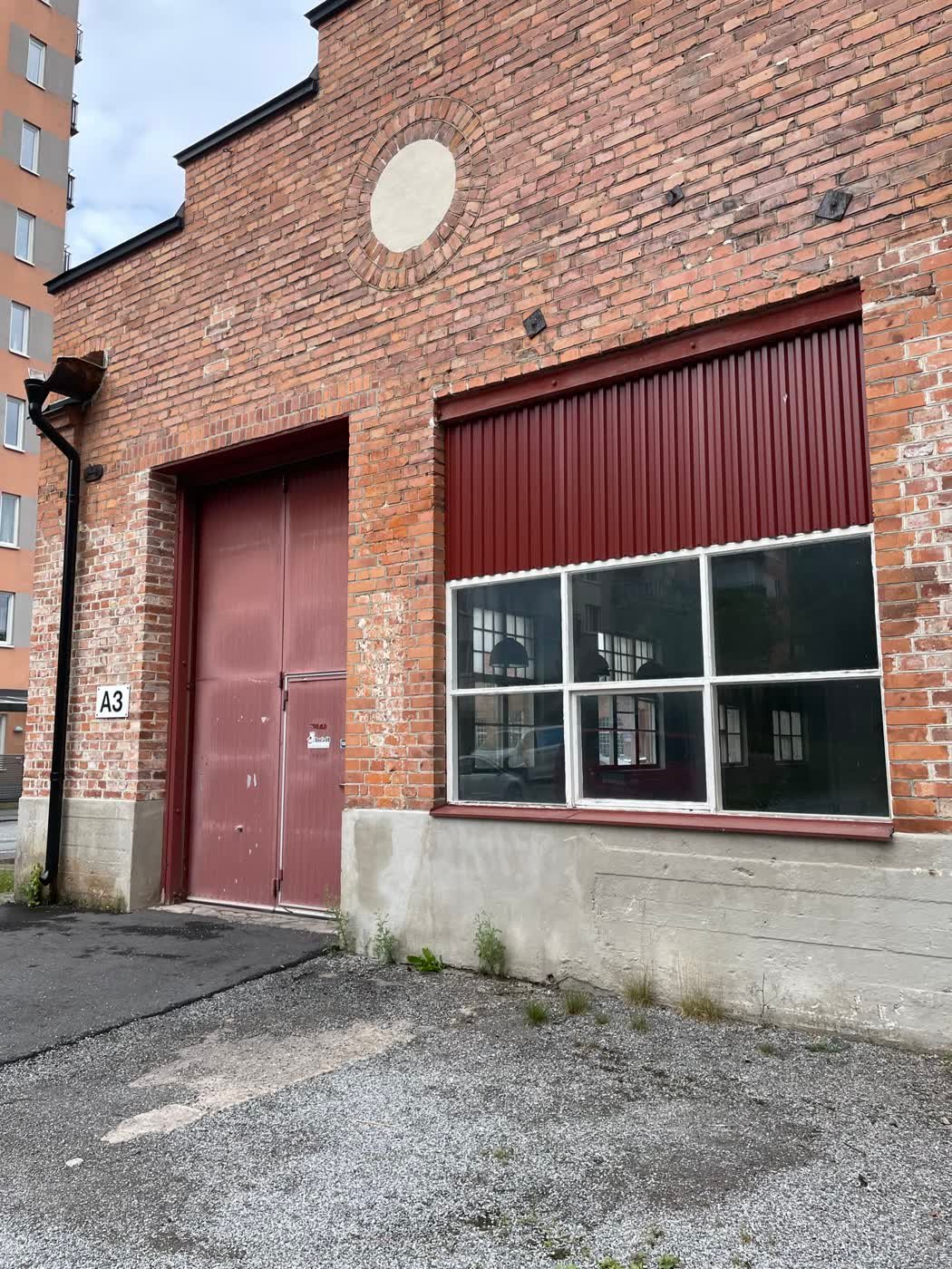 The workshop's red-brick facade - maroon loading doors and tall factory windows, unit A3.