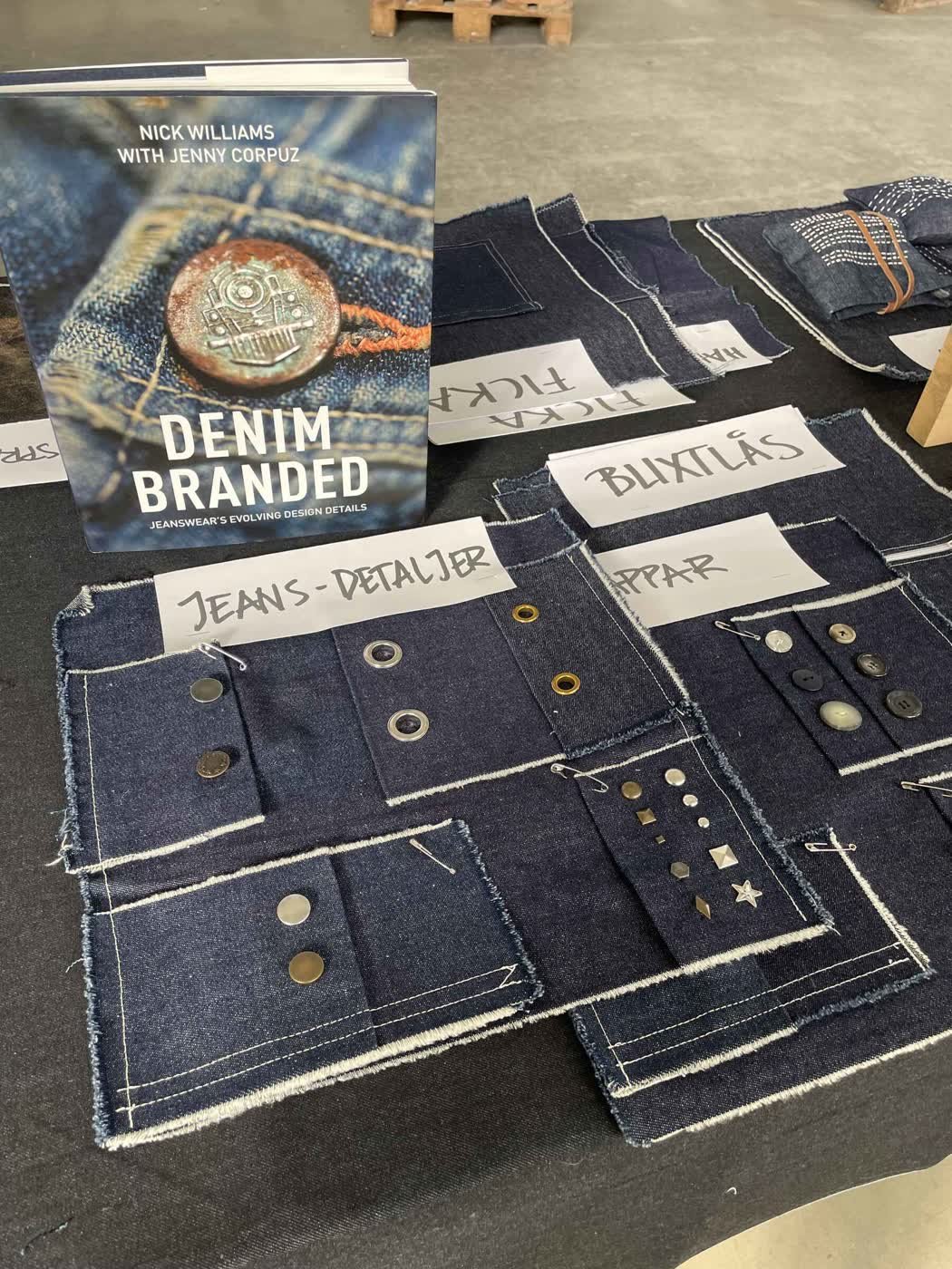 Denim swatches showing hardware - buttons, rivets and studs - beside the reference book "Denim Branded".